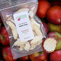 Packaged dehydrated apple chips with a label on a background of fresh apples.