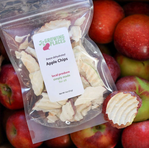Packaged dehydrated apple chips with a label on a background of fresh apples.