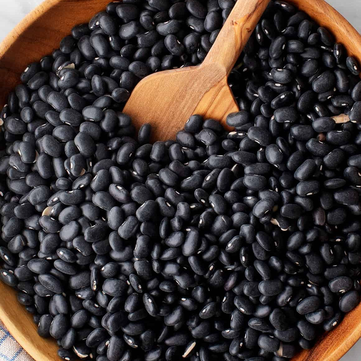 Wooden bowl filled with black beans and a wooden spoon on a light background